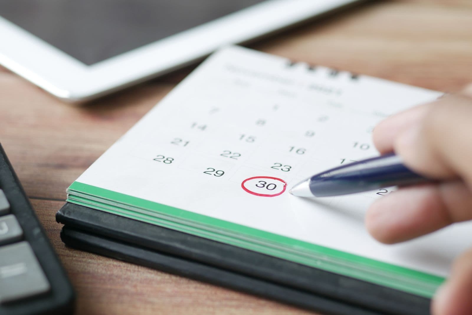 Eine Hand kreist mit dem Stift einen Tag auf einem Tischkalender ein